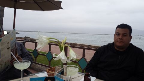 1996 Ford Bronco - Two people sit at a table with drinks and flowers, with a view of the ocean under a cloudy sky.
