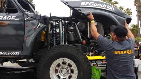 1996 Ford Bronco - Mechanic works on the engine of a custom off-road race truck, with the hood open revealing the complex mechanics.
