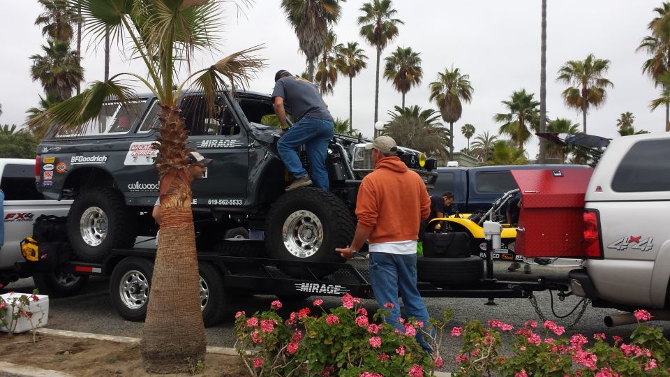 1996 Ford Bronco on a trailer, being worked on by two men. Another truck and trailer are visible
