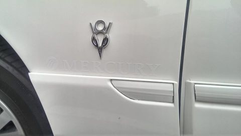 2000 Mercury Grand Marquis - A V8 emblem is affixed above the debossed 'MERCURY' text on the side of a white vehicle.