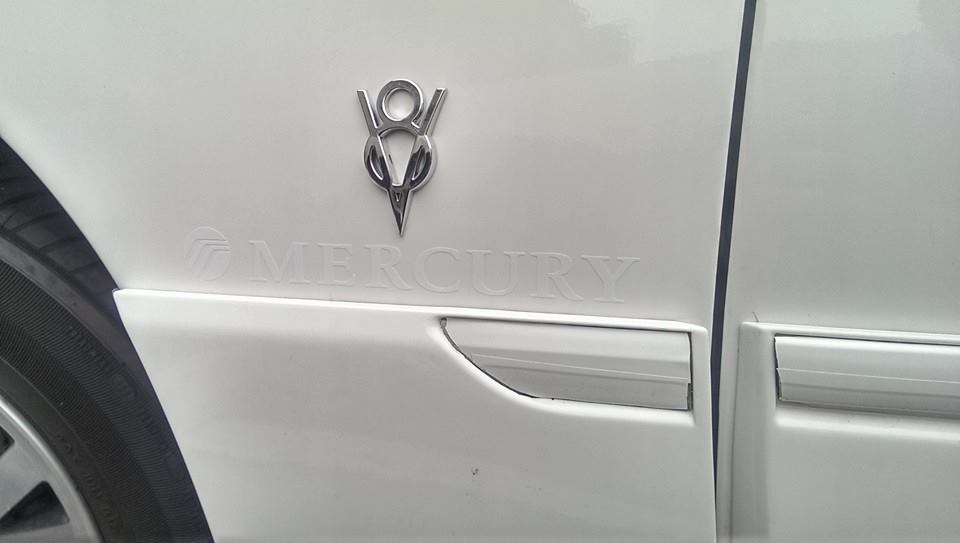 Close-up of a V8 emblem and 'MERCURY' text on a white car door