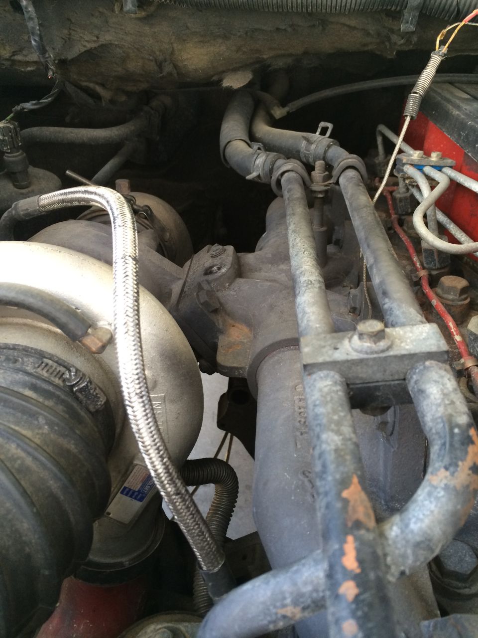 Engine bay with turbocharger, hoses, and metal pipes. Some parts are dirty and corroded