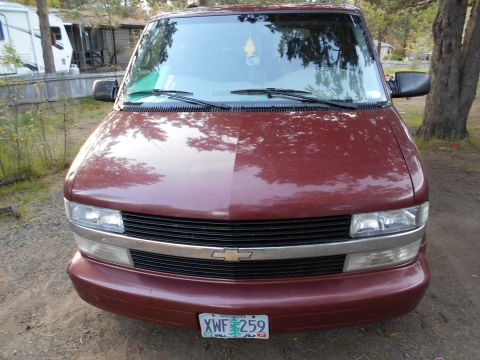 2000 Chevrolet Astro - The front of a maroon Chevrolet Astro van is shown parked outdoors with trees and a trailer in the background.