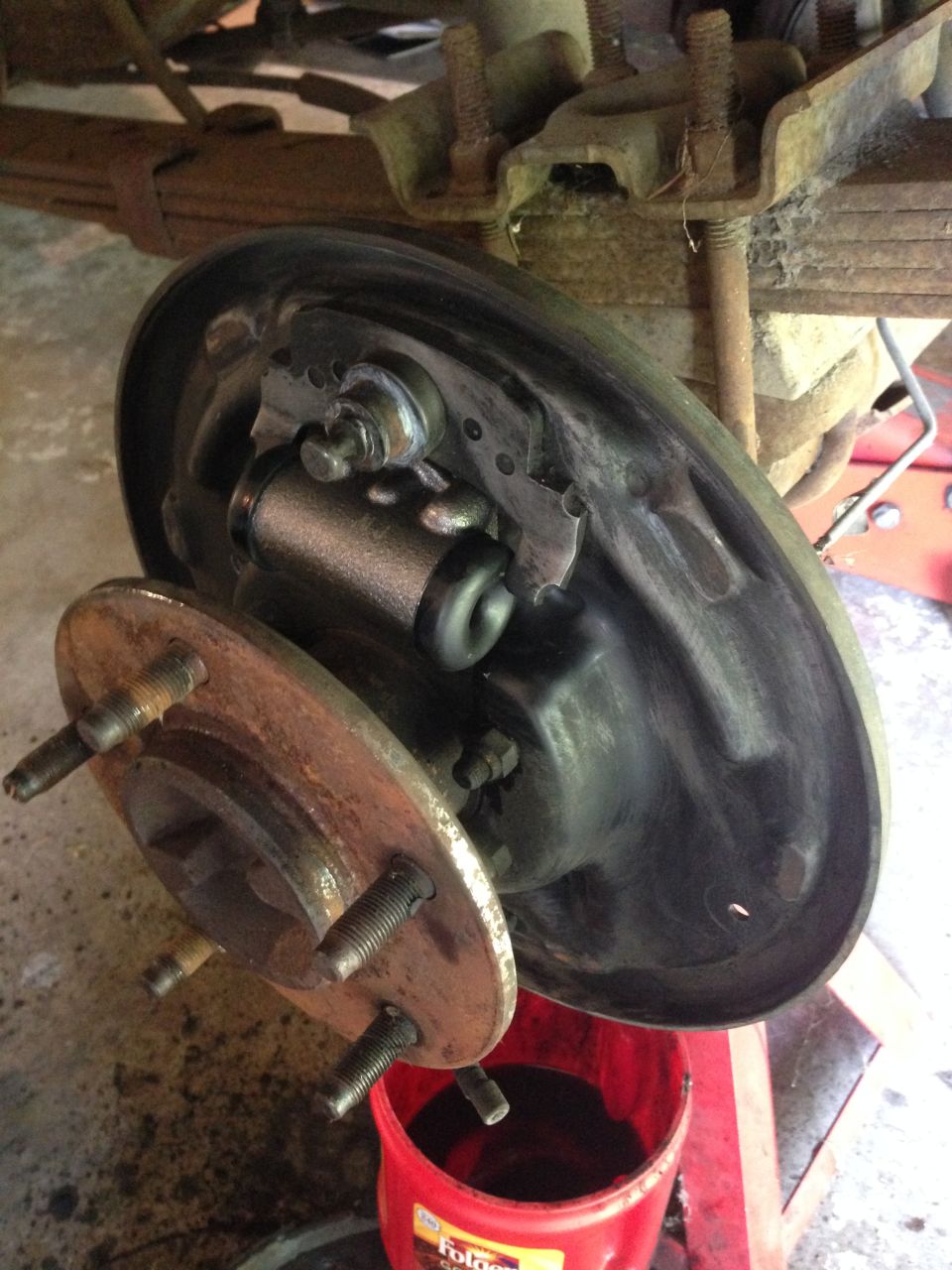 Rusty wheel hub and brake drum assembly with brake cylinder and shoes, resting on a red bucket