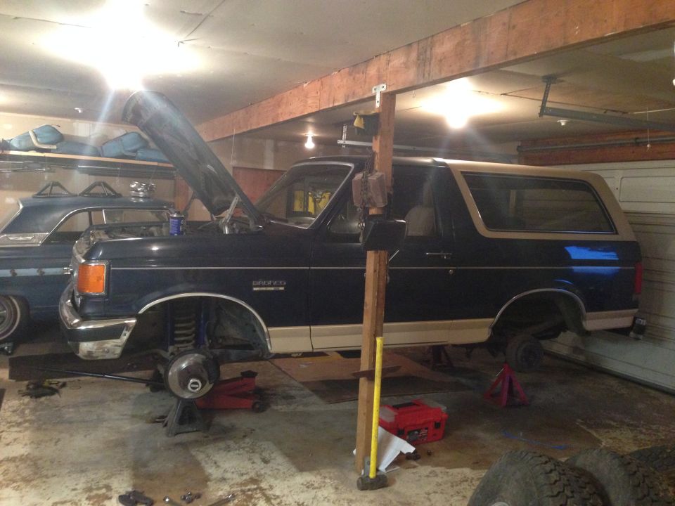 1990 Ford Bronco side view, dark blue and tan, hood open, on jack stands