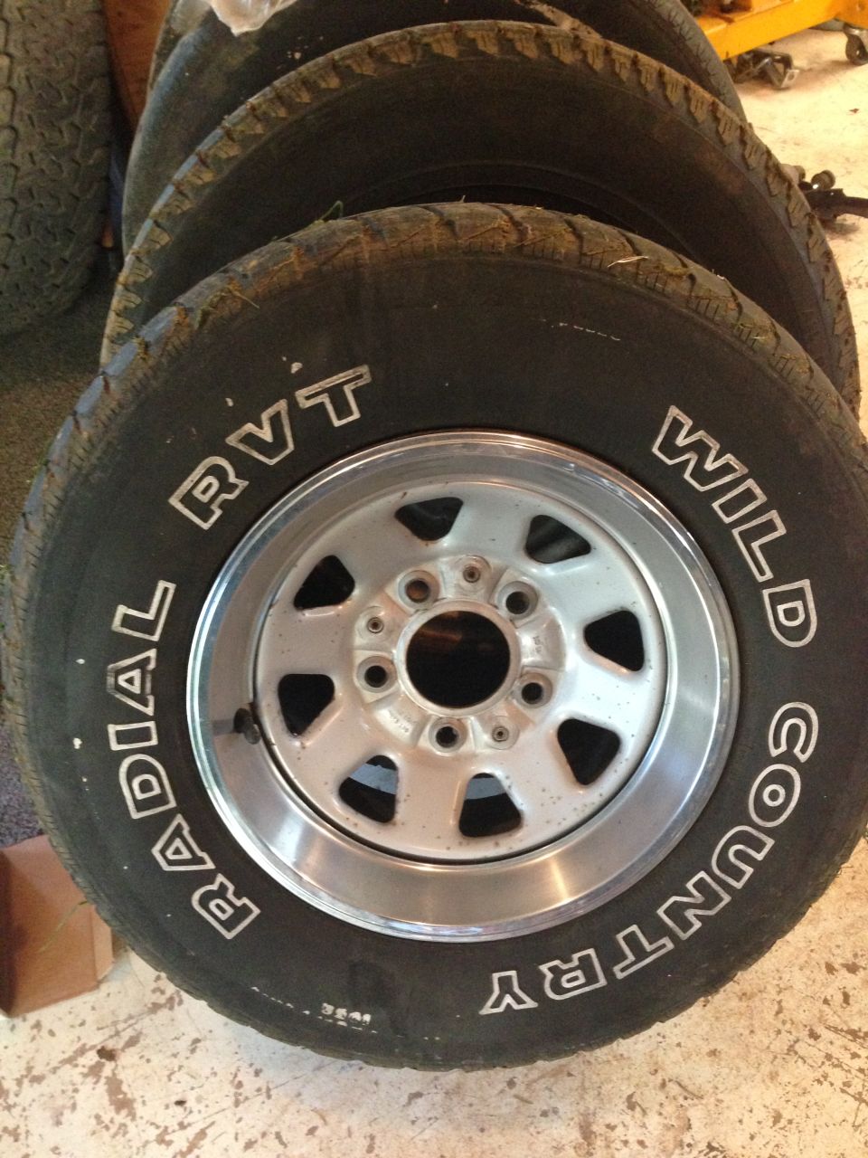 Four tires with silver rims stacked, showing 'Wild Country Radial RVT' text