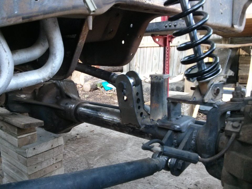 Close-up of vehicle's front axle, suspension, and exhaust headers, possibly during a modification