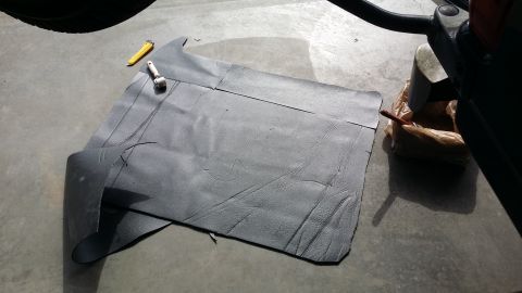 1994 Ford Bronco - Sound deadening material is laid out on a concrete floor, ready for installation, with a roller and utility knife nearby.