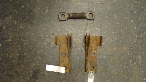 1979 Ford Bronco - Vehicle suspension components, including two brackets and a connecting rod, are laid out on a textured surface.