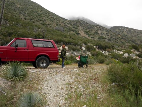 1988 Ford Bronco - Red 1988 Ford Bronco parked on a dirt road with a person and camping chairs in a mountainous landscape.