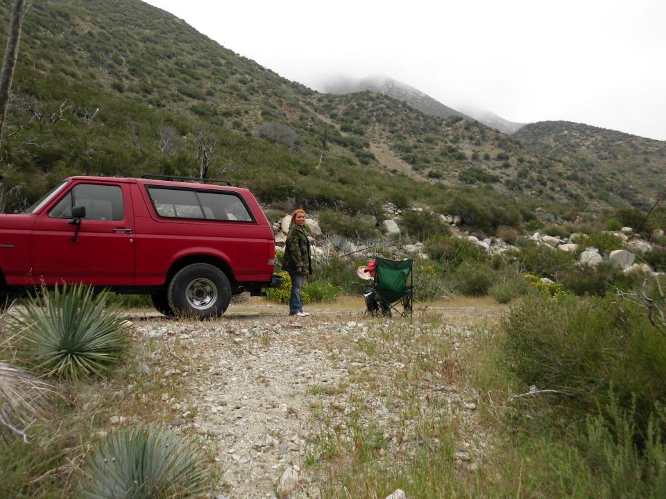1988 Ford Bronco parked on a dirt road in a mountainous area. A person stands next to the vehicle
