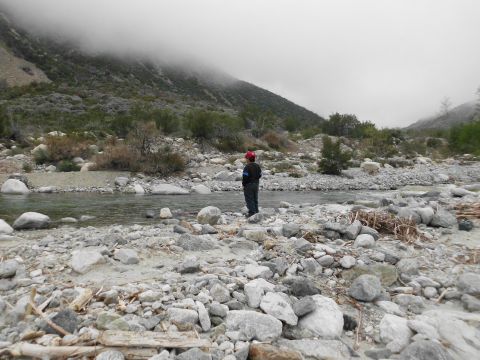 1988 Ford Bronco - A person stands in a rocky riverbed, surrounded by sparse vegetation and mountains shrouded in fog.