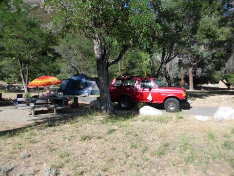 1988 Ford Bronco - A red SUV is parked at a campsite with a tent and picnic table set up under trees.