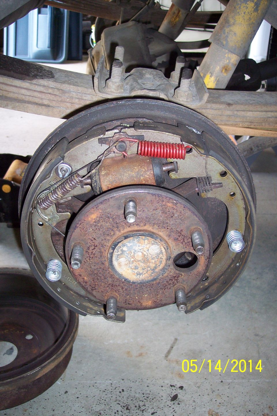 close-up of a rusty rear brake drum assembly with new red spring