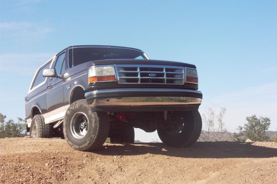 Low front view of lifted brown Ford Bronco on a desert dirt berm, axle visible