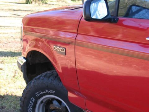 1992 Ford Bronco - Side view of a red 1992 Ford Bronco, its distinctive body lines and fender badge.