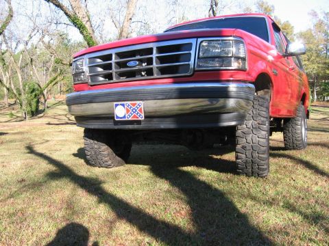 1992 Ford Bronco - This red 1992 Ford Bronco is shown from a low front angle, highlighting its lifted suspension and off-road tires.