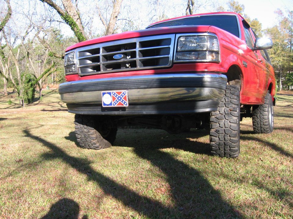 Front view of a red 1992 Ford Bronco with large tires, parked on grass