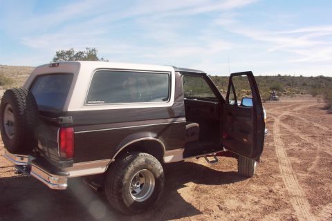 1992 Ford Bronco - Rear view of a 1992 Ford Bronco with doors open, parked off-road in a desert setting.