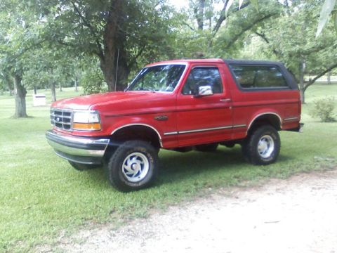 1992 Ford Bronco - Red lifted full-size Ford Bronco with black hardtop and chrome wheels parked on a grassy yard.