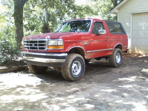 1992 Ford Bronco - A red 1992 Ford Bronco is parked outside a garage on a sunny day.