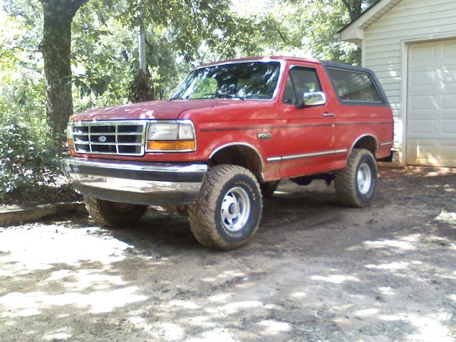 Red 1992 Ford Bronco parked in a dirt driveway next to a garage