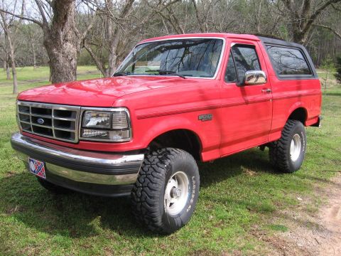 1992 Ford Bronco - This red 1992 Ford Bronco is shown from a 3/4 front angle, parked on a grassy area.