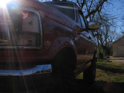 1992 Ford Bronco - A red pickup truck is parked outdoors with trees and a building in the background.