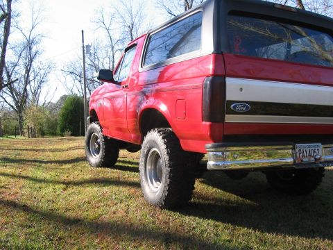 1992 Ford Bronco - This red 1992 Ford Bronco features a lifted suspension and aftermarket wheels, seen from a rear three-quarter perspective.
