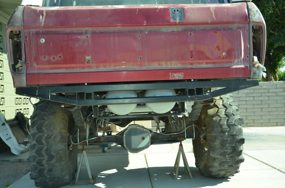 rear of red pickup truck with large off-road tires, custom bumper, and dual propane tanks underneath