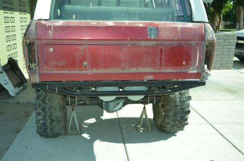 1979 Ford Bronco - Rear view of a red SUV with custom bumper and large tires, missing taillights and supported by jack stands.