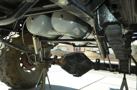 1979 Ford Bronco - The undercarriage of a vehicle is shown, large propane tanks and heavy-duty suspension components.