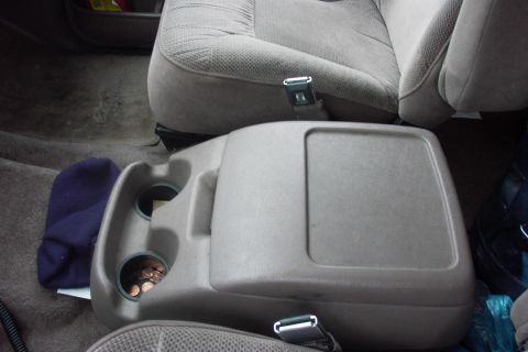 1992 Ford Bronco - Interior shot looking down at a tan/gray removable center console with lidded storage bin and two cup holders holding loose change, flanked…