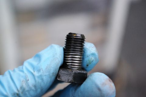 1995 Ford Bronco - A close-up shows a bolt being held by a hand wearing a blue glove. The bolt has visible threads and some grease.