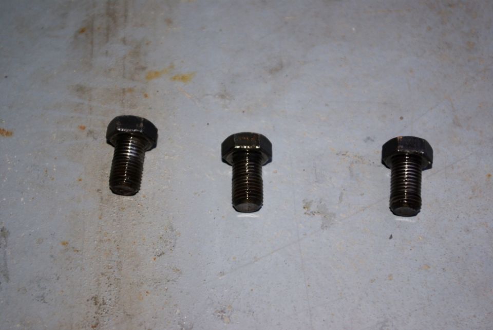 Three hex head bolts on a gray surface. A "SUPERMOTORS" logo is in the lower right corner