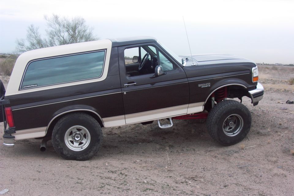 1992 Ford Bronco with aftermarket wheels and lift kit parked on dirt
