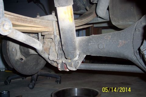 1978 Ford Bronco - Close-up view of the rear suspension and axle of a vehicle, with a rolling office chair beneath.