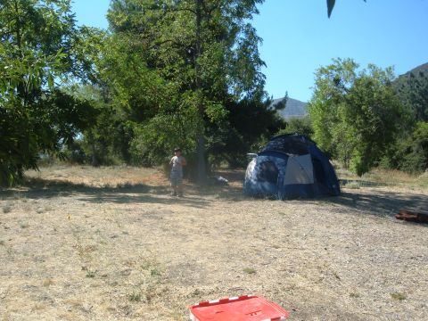 1988 Ford Bronco - A blue tent is set up at a campsite with a person standing nearby under a tree.