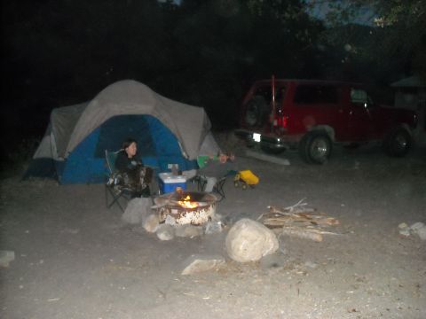 1988 Ford Bronco - A red SUV is parked at a campsite with a tent and campfire in the foreground.