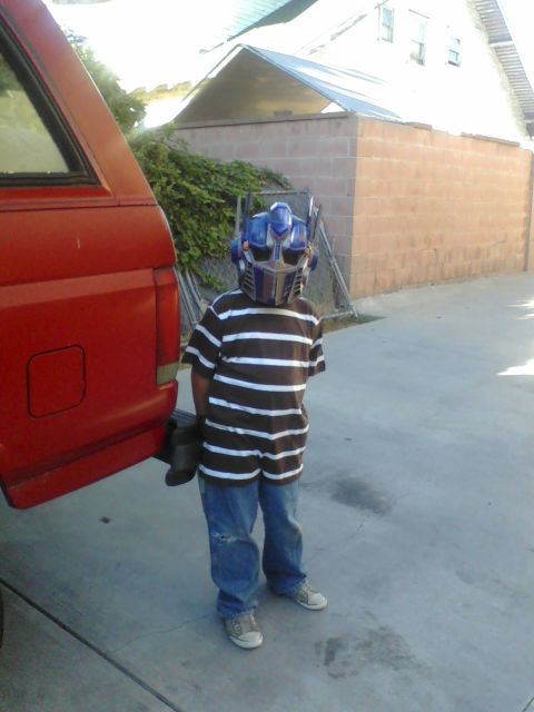 1988 Ford Bronco - A child in an Optimus Prime mask stands next to the side of a red SUV.