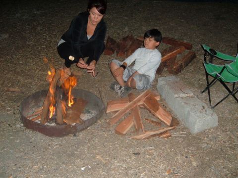 1988 Ford Bronco - A woman roasts a marshmallow over a campfire while a boy sits nearby with firewood and camping chairs.