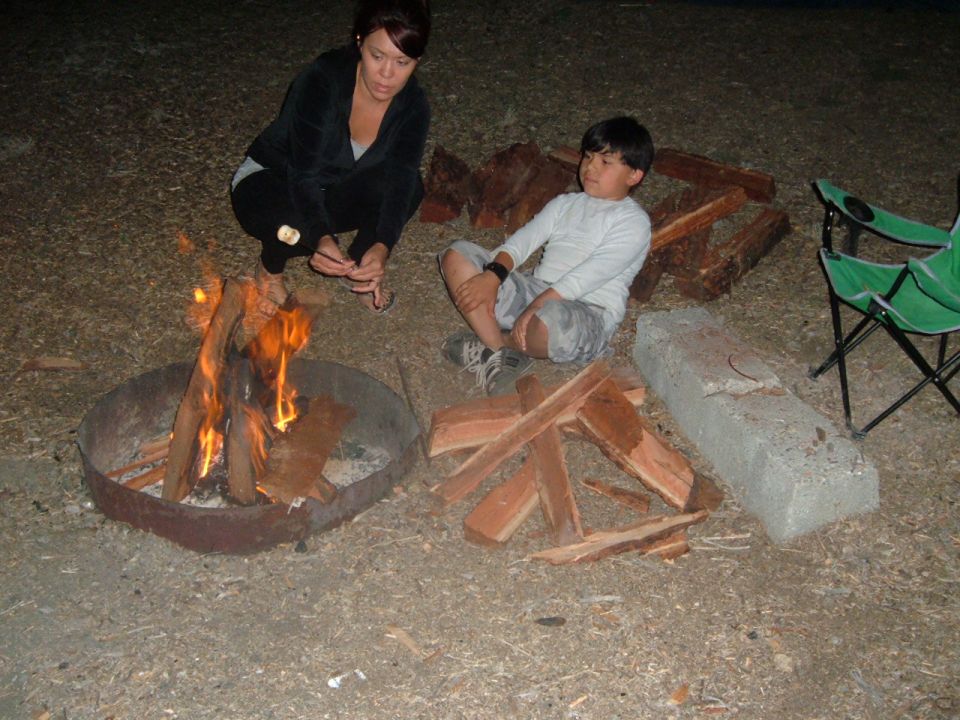 Campfire scene with two people, firewood, and camping chairs