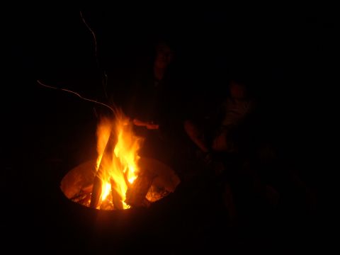 1988 Ford Bronco - A campfire burns brightly in the dark, with figures gathered around it.
