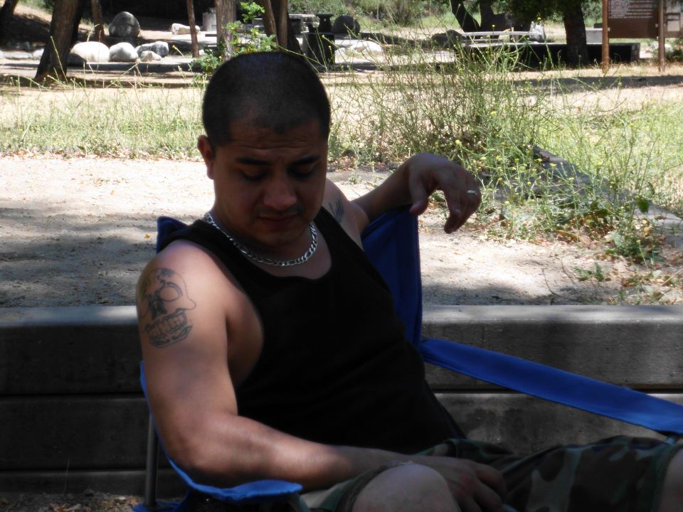 Man in black tank top and camouflage shorts sits in a blue camping chair outdoors