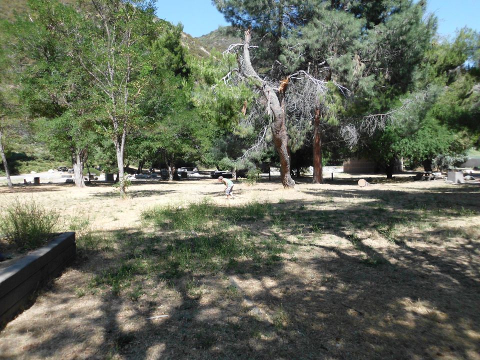 Campsite scene with trees, dry grass, and a distant person. Watermark reads SUPERMOTORS.NET