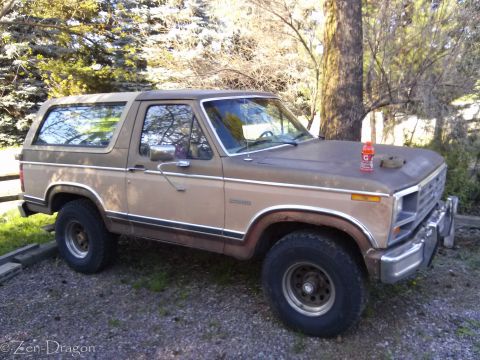 1990 Ford Bronco - This two-tone brown SUV is parked on a gravel surface with trees in the background.