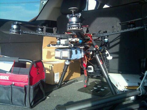 1986 Ford Bronco - A large drone is packed in the cargo area of a vehicle, alongside a toolbox and boxes.