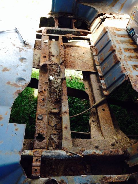 1979 Ford Bronco - The vehicle's interior floor pan and frame are severely corroded, with significant rust and holes exposing the ground beneath.