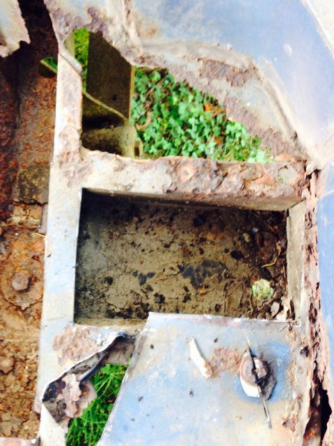 1979 Ford Bronco - Heavily rusted metal frame with holes, revealing grass and dirt below.