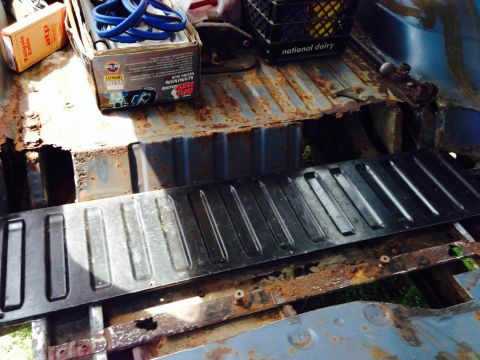 1979 Ford Bronco - The interior cargo area of a vehicle shows significant rust damage and a black metal floor panel.